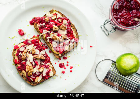 Toast mit Erdnussbutter, hausgemachte Marmelade himbeere Chia, Walnüsse, Mandeln und Sonnenblumenkerne auf weißem Hintergrund. Gesunde Idee zum Frühstück Stockfoto