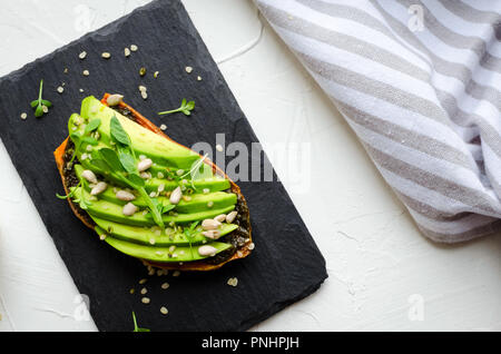 Gesunde avocado Toasts auf die süßkartoffel für Frühstück oder Mittagessen mit vegan Pesto, microgreens, geschnitten, Avocado, Hanf und Sonnenblumen. Vegetarische Kost Stockfoto