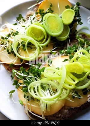 Nahaufnahme der gesunde vegetarische Sandwich aus Vollkornbrot, Schafskäse, Lauch, Butter, Keime, Sprossen auf grau, weiße Platte. Stockfoto