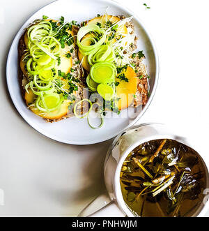 Nahaufnahme von vegetarisches Sandwich. Vollkornbrot, Schafskäse, Lauch, Butter, Keime, Sprossen und Becher Bergtee, Shepherd's Kaffee in Cat Becher Stockfoto