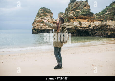 Mädchen mit einem Rucksack Touristen fotografieren eine schöne Landschaft an der Atlantikküste. Stockfoto