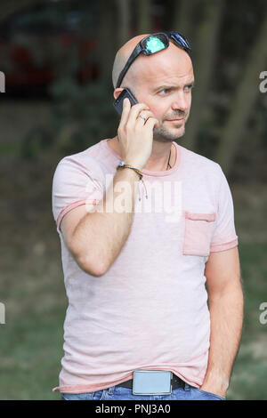 Der 41-jährige sportlich Mann arbeitet in Brandenburg in der Nähe von einem See mit Smartphone und Laptop. Stockfoto