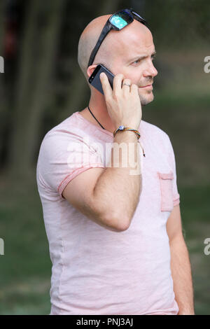 Der 41-jährige sportlich Mann arbeitet in Brandenburg in der Nähe von einem See mit Smartphone und Laptop. Stockfoto
