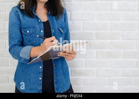 Frau Hände halten ein Notizbuch und einen Stift bereit, die Noten in der Nähe einer weißen Wand nehmen Stockfoto