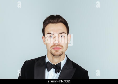 Portrait einer jungen gutaussehenden Mann im Smoking, ernst in die Kamera schaut, gegen Pl​ain studio Hintergrund. Stockfoto