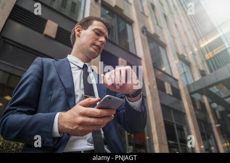 Nahaufnahme des Kaufmanns holding Handy in der Hand und Uhren. Stockfoto