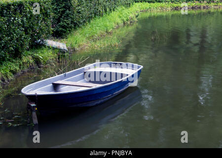 Einzelne leere alte blaue Boot in einem grünen Dickicht an einem trüben Teich günstig Stockfoto