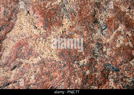 Unebene Oberfläche aus rosa Granit Boulder teilweise mit Sand bedeckt, kann als Hintergrund oder Textur verwendet werden. Stockfoto