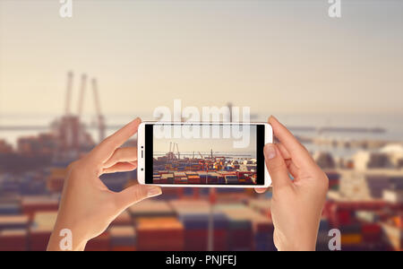 Ein Tourist ist ein Foto von Sea Port Terminal mit Kränen, Schiffe, die für das Entladen und eine große Anzahl von Containern auf einem Mobiltelefon Stockfoto