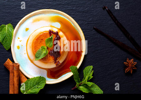 Essen Dessert Konzept hausgemachte Vanille Karamell Pudding oder Panna cotta mit Vanille und Gewürzen auf schwarzen Stein Hintergrund Stockfoto