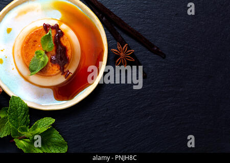 Essen Dessert Konzept hausgemachte Vanille Karamell Pudding oder Panna cotta mit Vanille und Gewürzen auf schwarzen Stein Hintergrund Stockfoto