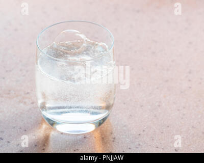 Gasblasen in Glas mit Mineralwasser mit Kohlensäure auf rosa Board Stockfoto