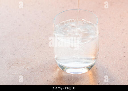 Natürliche kohlensäurehaltige Wasser gießt in Glas auf rosa Board Stockfoto