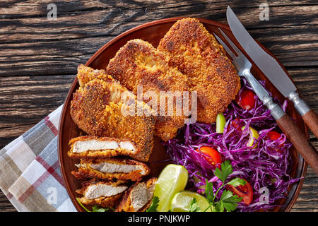 Blick von oben auf die knusprigen Schweinekoteletts mit leckerem Rotkohl, Kalk und Petersilie in einem Ton Platte auf kariert Serviette auf einem hölzernen Tisch platziert, rustikaler Stil, Clo Stockfoto