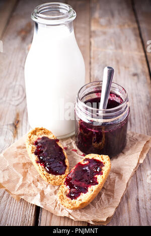 Schwarze Johannisbeere Konfitüre in Glas, Milch und Kekse auf rustikalen Holzbrett Stockfoto