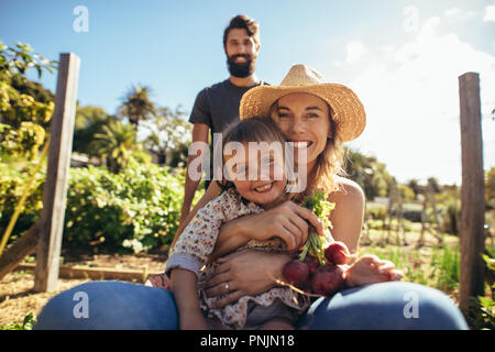 Porträt der schönen Frau mit ihrer Tochter sitzen in Schubkarre während man drücken. Lächelnden jungen Mutter und Tochter genießen in der Schubkarre fahren Stockfoto