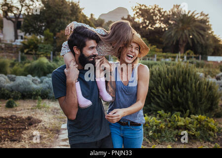 Bart Mann, der kleine Mädchen auf der Schulter mit Frau am Bauernhof lachen. Schöne Familie von drei Spaß auf ihrer Farm. Stockfoto