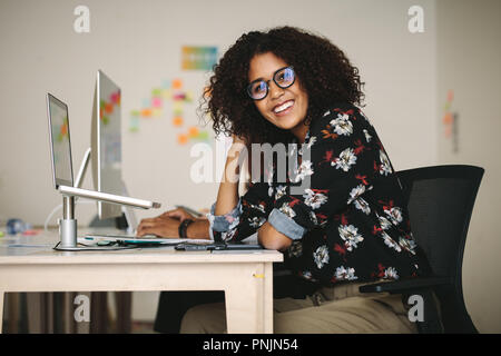 Lächelnd geschäftsfrau an Ihrem Schreibtisch im Büro mit einem Laptop auf einem Stativ montiert. Frau mit Brille arbeiten am Laptop im Büro. Stockfoto