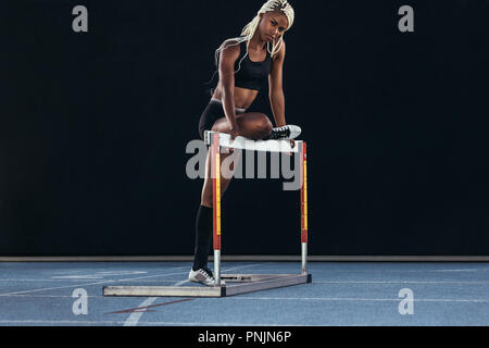 Weibliche Athleten auf der Laufstrecke ein Bein auf eine Hürde. Stockfoto
