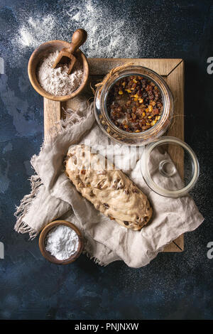 Christmas Cake, traditionelle deutsche Festliches backen. Vollkorn Teig stollen Vorbereitung auf Leinen Serviette mit Schalen von Mehl und Rosinen über Dunkelblau Stockfoto