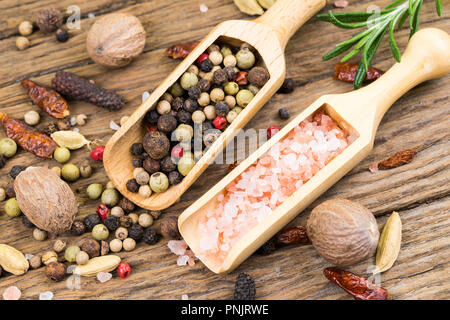 Nahaufnahme der bunte Pfefferkörner und rosa Kristall Salz auf kleinen hölzernen Spice Lufthutzen auf rustikalen Holz Hintergrund mit einem Zweig Rosmarin in der backgroun Stockfoto