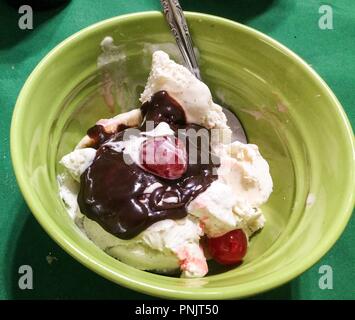 Eis mit Banane, Kirsche und Hot fudge Sauce in Hellgrün Darms mit Löffel auf dunkelgrünem Hintergrund. Stockfoto