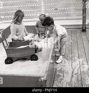 1960, historische, junge Kinder zusammen draußen spielen in einem Holz- Sandkasten und mit einem Metall, Holz- fourway playtruck, England, UK. Stockfoto