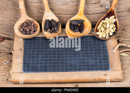 Nahaufnahme von vier hölzernen Kochlöffel mit verschiedenen exotischen Gewürzen und einem alten Schiefer Tafel für die Kennzeichnung auf einem rustikalen Holzmöbeln Hintergrund Stockfoto