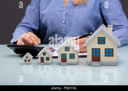 Zeile der zunehmenden Haus Modelle Vor Geschäftsfrau Berechnung Rechnung auf Schreibtisch Stockfoto