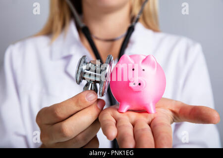 Nahaufnahme der Hand einer Ärztin Untersuchen rosa Sparschwein mit Stethoskop Stockfoto