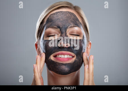 Close-up eine glückliche Frau mit Aktivkohle Maske auf grauem Hintergrund Stockfoto