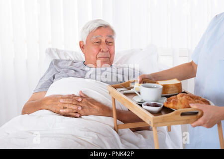 Junge weibliche Krankenschwester mit Speisen zu den älteren männlichen Patienten Stockfoto