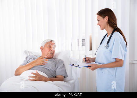 Junge weibliche Krankenschwester mit Zwischenablage Besuchen ältere männliche Patienten Stockfoto