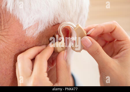 Die Ärztin Hand einfügen Hörgerät im Ohr von männlichen Patienten Stockfoto