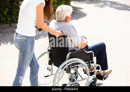 Junge Frau bei ihrem behinderten Vater auf Rollstuhl an im Freien Stockfoto