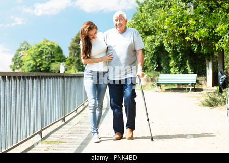 Junge Frau die Unterstützung Ihrer glücklichen Vater bei einem Spaziergang in der Nähe von Geländer in Park Stockfoto