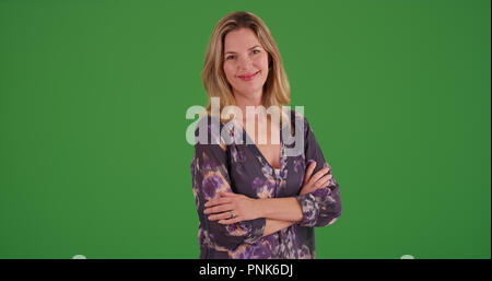 Kaukasische Frau mit verschränkten Armen in die Kamera lächeln auf Green Screen Stockfoto
