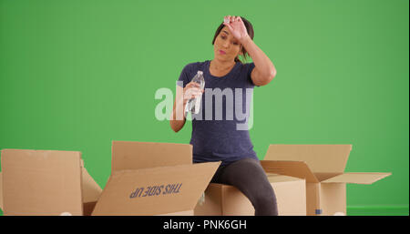 Latina Frau, die Pause vom Auspacken der Kartons Trinkwasser auf Green Screen Stockfoto