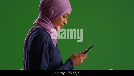 Profil von junge schwarze Frau, tragen, hijab SMS auf Handy auf Green Screen Stockfoto