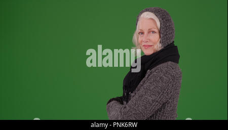 Charmante ältere Frau im Winter Kleidung mit Arme auf Green Screen gekreuzt Posing Stockfoto