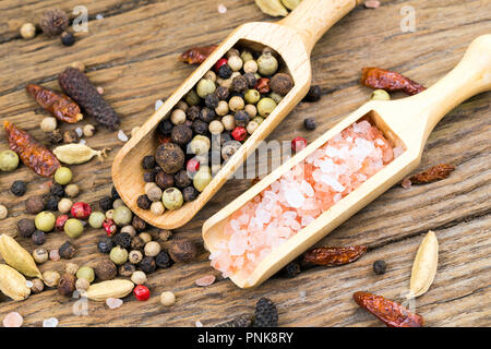 Nahaufnahme der bunte Pfefferkörner und rosa Kristall Salz auf kleinen hölzernen Spice Lufthutzen auf rustikalen Holz Hintergrund mit weiteren Gewürzen Stockfoto