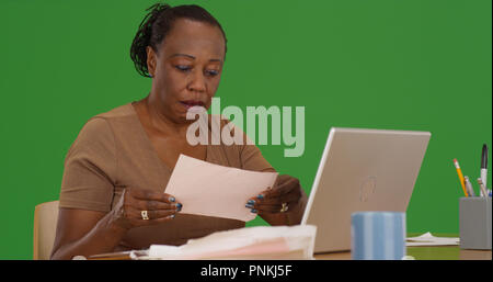 Ältere schwarze Frau tun Steuern am Schreibtisch sitzt mit Laptop auf dem Green Screen Stockfoto
