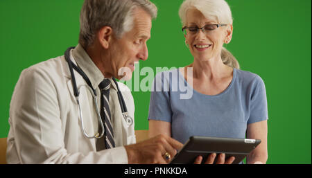 Doktor gehen über die Gesundheit der älteren Frau mit Tablette auf Green Screen Stockfoto