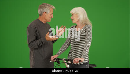 Alter Mann chatten mit alten Frau auf Fahrrad auf Green Screen Stockfoto