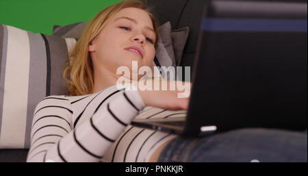 Closeup Portrait von blonde Frau liegend mit Laptop auf der Couch auf Green Screen Stockfoto
