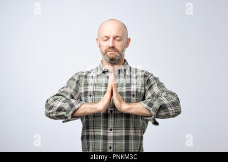 Yoga und Meditation. Stattliche glatzköpfige Mann mit Borsten halten die Augen geschlossen während der Meditation, entspannt, ruhig, friedlich, Hände halten in Schlamm Stockfoto