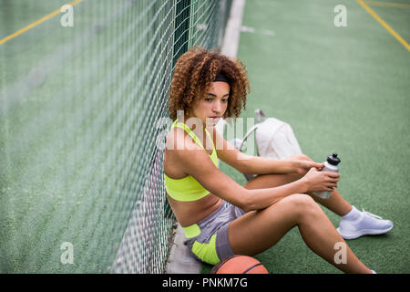 Junge erwachsene Frau sitzt auf einem Basketballplatz Stockfoto