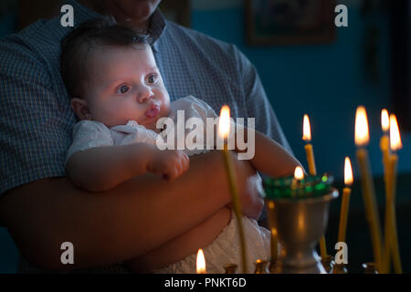 Die Hände des Vaters halten Sie das Baby in seinen Armen in der Kirche. Das Kind sieht auf die Kerzen brennen in den Tempel. Kind in der Kirche Stockfoto