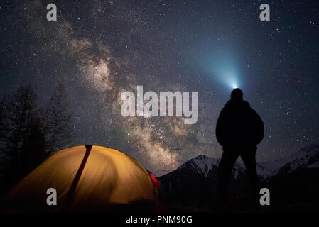 Man Touristen mit Taschenlampe steht in der Nähe von seinem Lager Zelt in der Nacht unter einem Himmel voller Sterne. Stockfoto