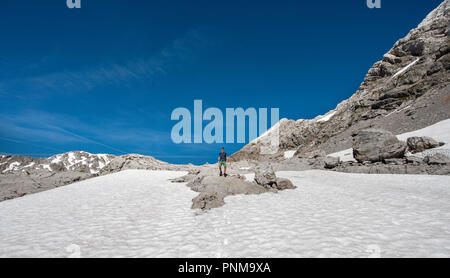 Wanderer steht auf Felsen im Schneefeld, Wanderweg zur Wasseralm über Niederbrunnsulzen, Steinernes Meer im Frühling mit Schnee Stockfoto